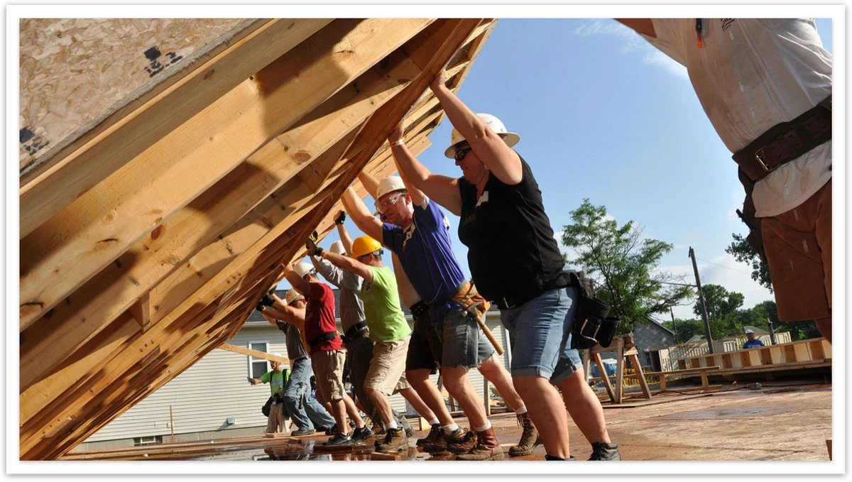 Volunteers raising a framed wall together at a home build